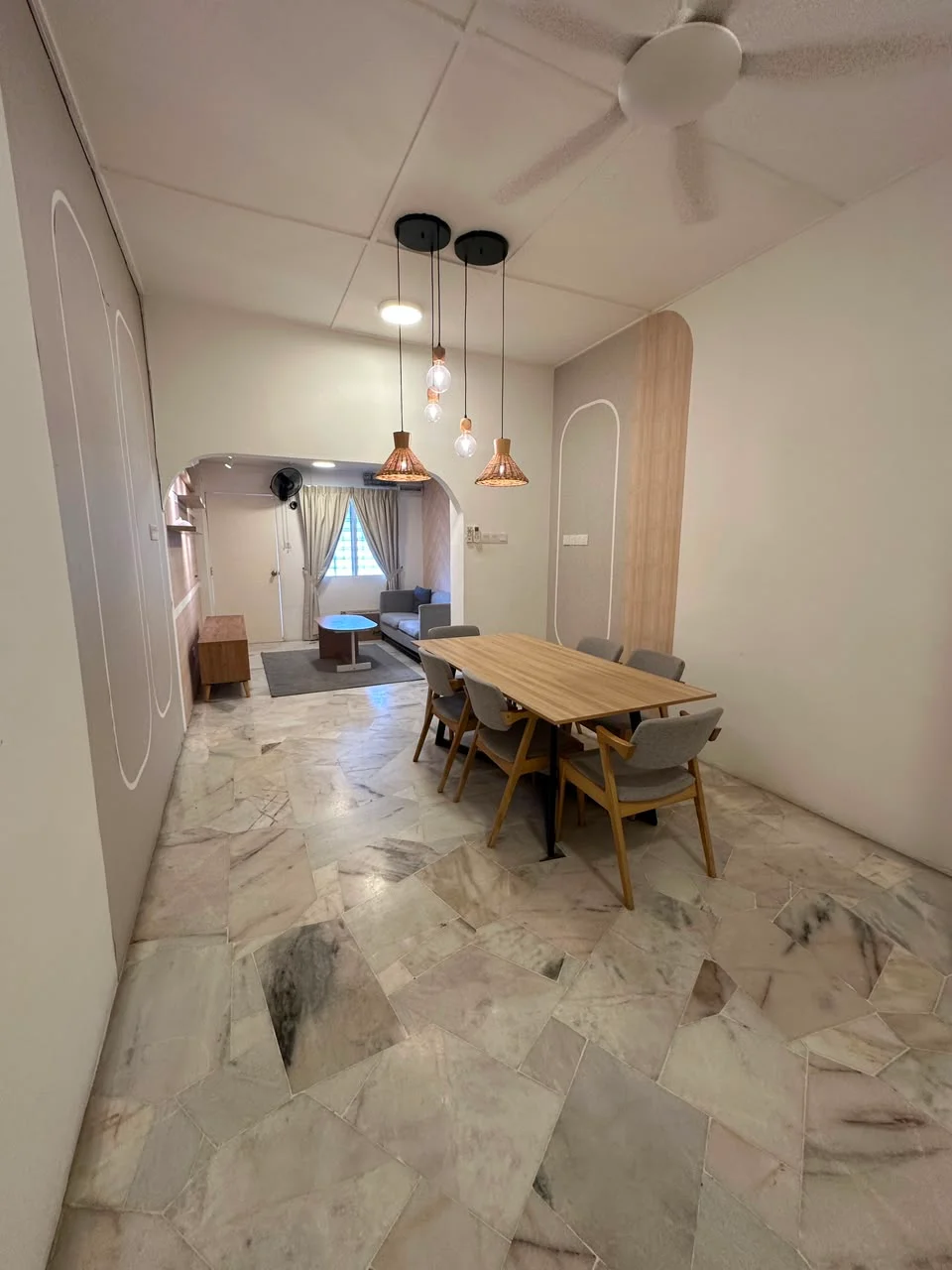 Dining features: dining table with wooden surface, 4 upholstered dining chairs, pendant lights with copper finish, marble flooring, white painted walls, ceiling fan, window with sheer curtains, open layout to living area; style: modern. Living features: sofa visible in background, coffee table visible in background, area rug visible in background, floor-to-ceiling window, curtains visible in background; style: modern.